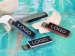 USB-Sticks in Blau, Schwarz und Rot mit Platz für individuelles Logo, auf buntem Untergrund platziert.