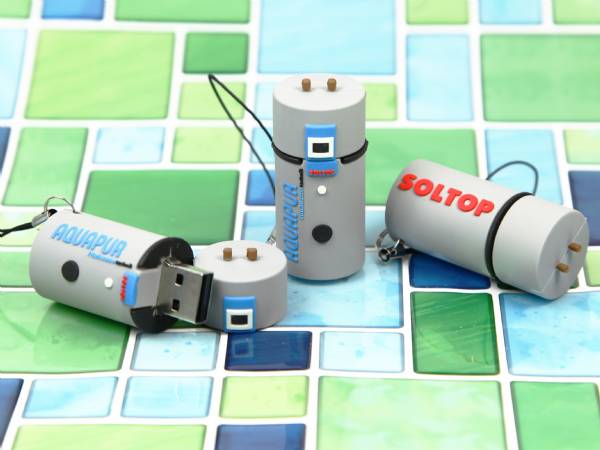 Drei USB-Sticks in Form von Heizungen, bedruckt mit den Logos AQUAPUR und SOLTOP, auf buntem Fliesenhintergrund.