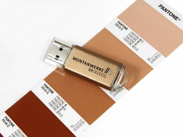 USB-Stick in Gold mit individueller Beschriftung und PANTONE-Farbmustern im Hintergrund. Ideal für Werbezwecke.