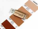 USB-Stick in Gold mit individueller Beschriftung und PANTONE-Farbmustern im Hintergrund. Ideal für Werbezwecke.