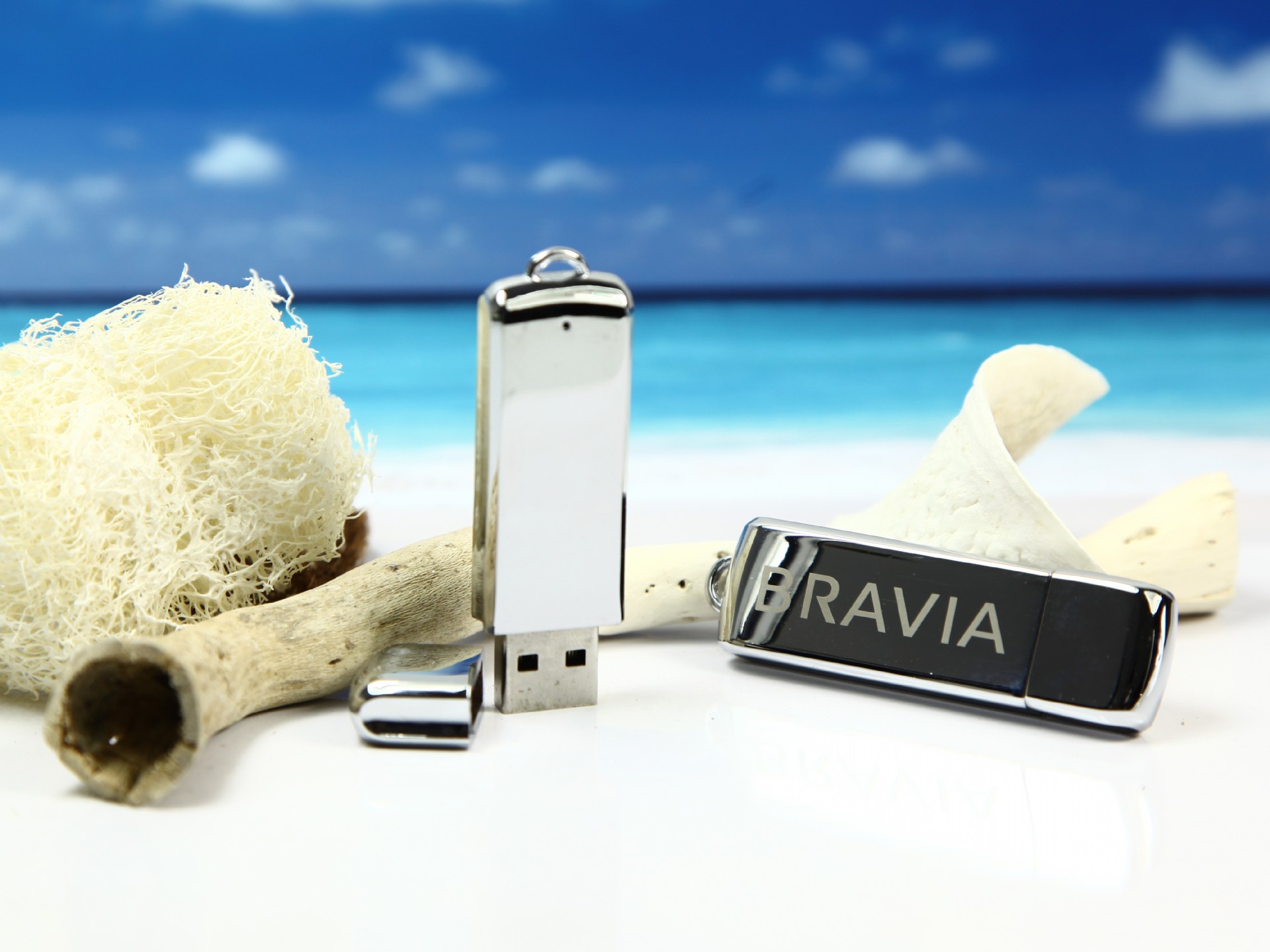 USB-Sticks in schimmerndem Design, platziert auf hellem Sand und maritime Dekorationen. Ideal für Promotions und Branding.